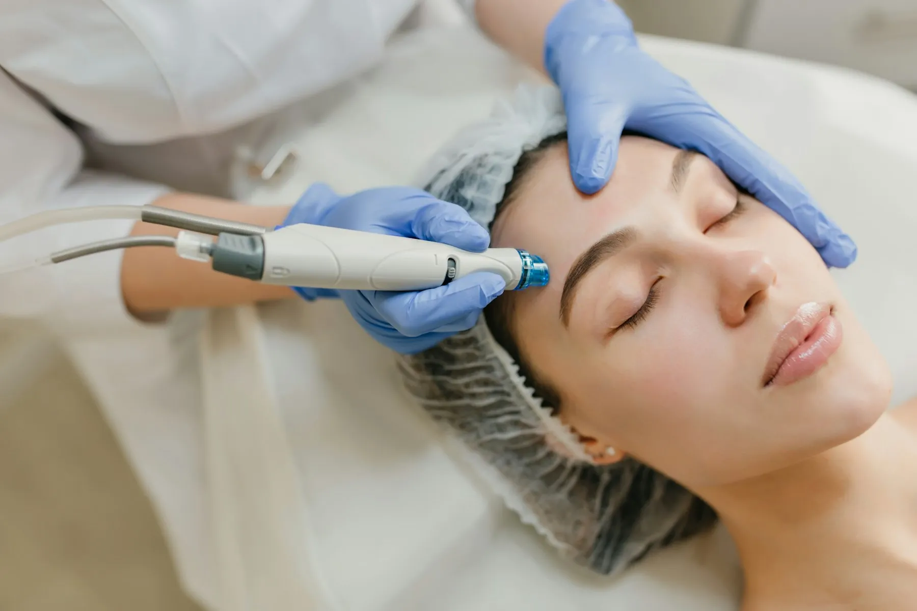 A gloved practitioner using a handheld skin device on a relaxed patient