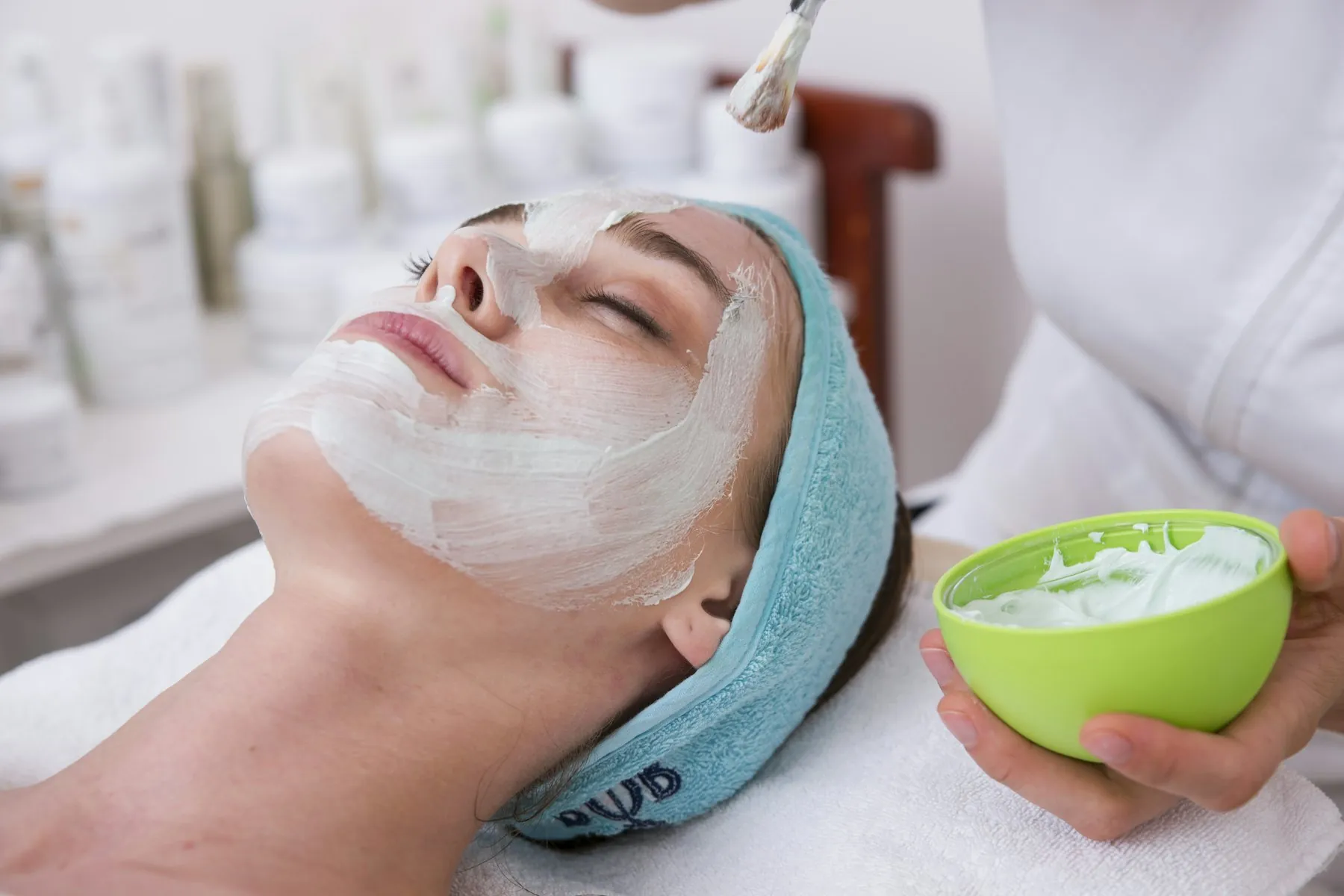 A woman relaxing in a teal headband with a cream mask being applied