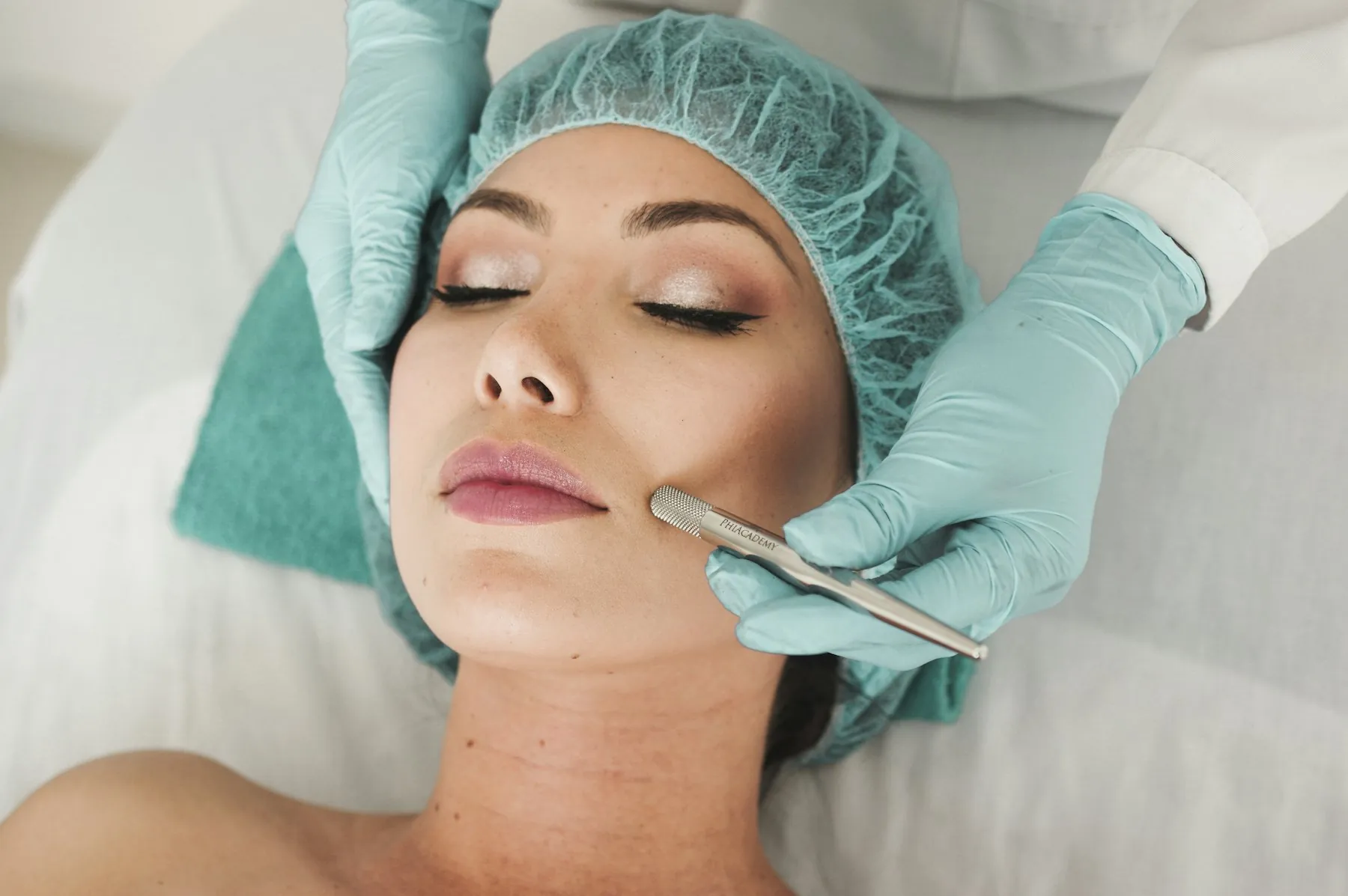 A practitioner in gloves guiding a treatment tool along a patient's cheek