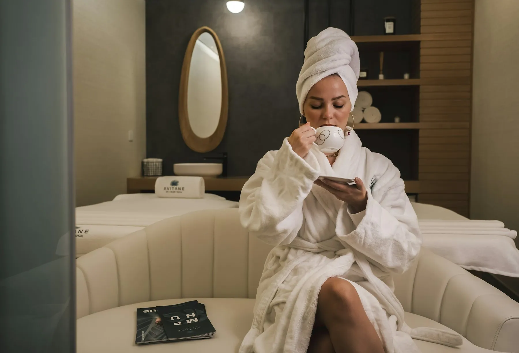 A woman in a white robe sipping tea in a softly lit spa lounge