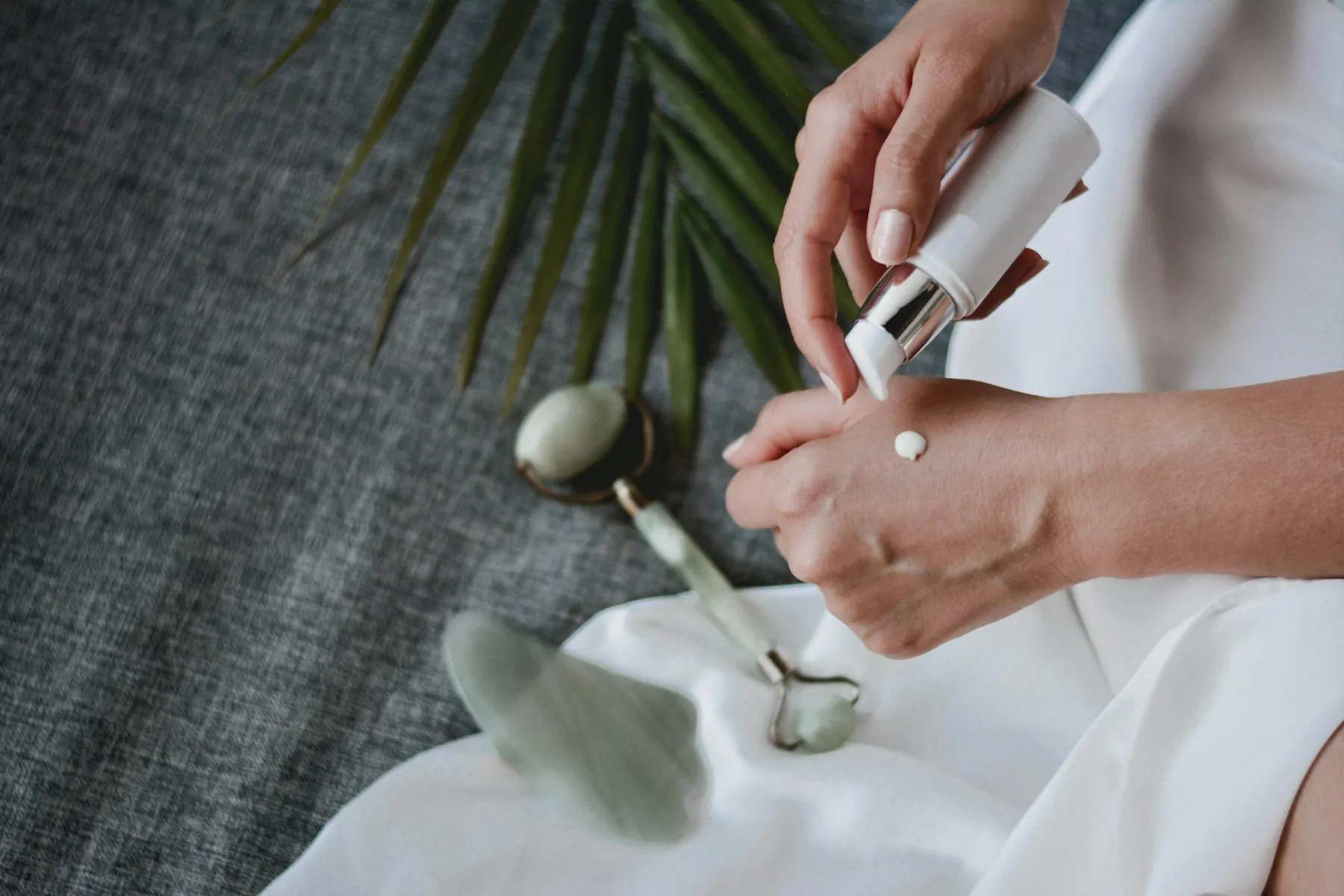 Hands applying serum beside a jade roller and gua sha stone